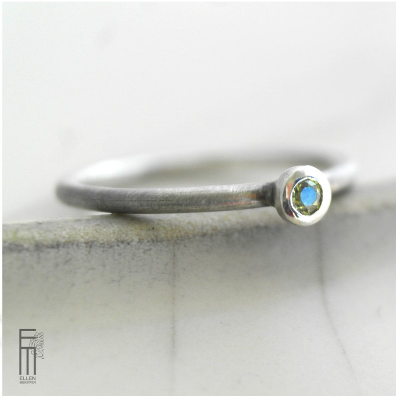 May include: A silver ring with a small, round, blue and green gemstone.