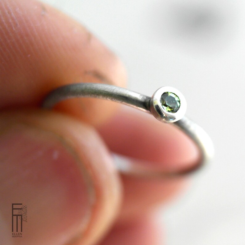 May include: A silver ring with a small, round, green gemstone set in a bezel setting.