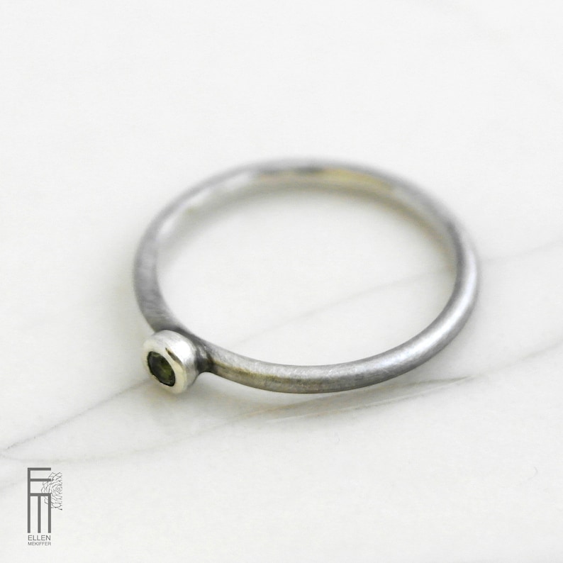 May include: A silver ring with a small, round, green gemstone set in the band.