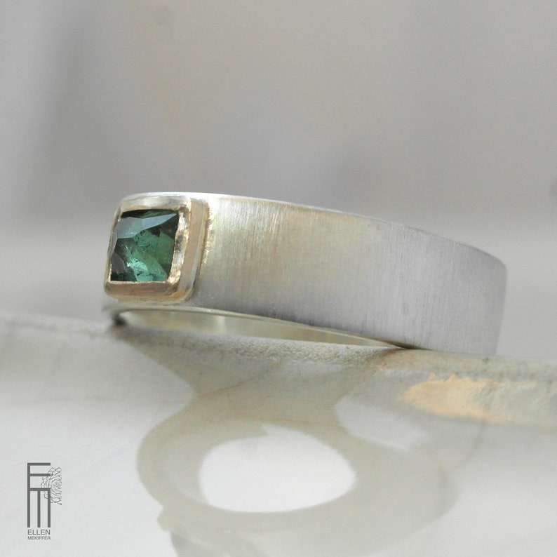May include: A silver band ring with a brushed finish and a square green gemstone set in a gold bezel.