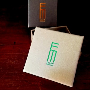 May include: A white box with a green logo that says "Ellen Mekiffer" and the letters "EM" in a stylized font.