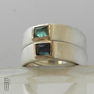 May include: Two silver rings with a brushed finish, each set with a square green gemstone. The rings are stacked on top of each other.