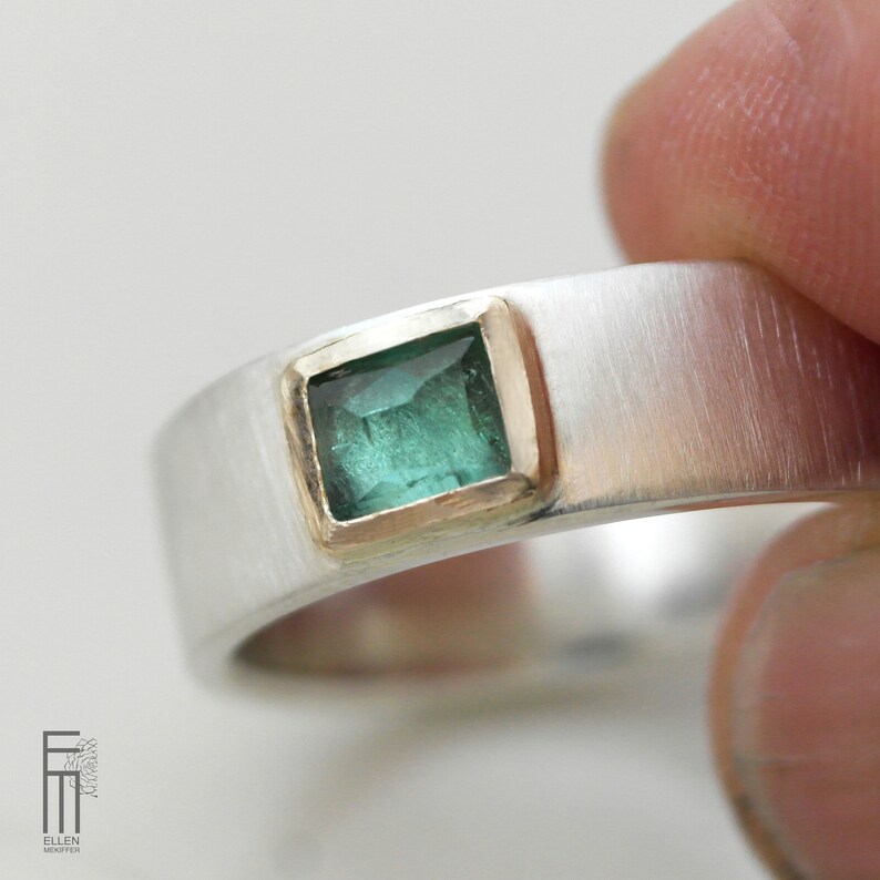 May include: A silver band ring with a square emerald green gemstone set in a gold bezel.