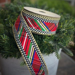 May include: A spool of wired ribbon featuring a vibrant red, green, and blue plaid pattern. The edges of the ribbon are decorated with a black and white checkered border and a thin gold metallic trim, creating a distinct contrast in colors.