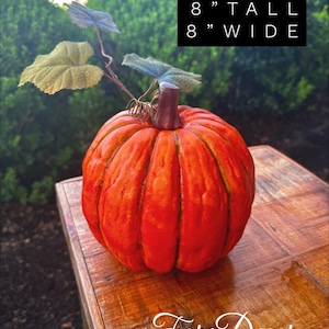 May include: An orange pumpkin with a stem and leaves, 8 inches tall and 8 inches wide, sits on a wooden table. The pumpkin is a fall decoration. The text "Fore Decor" is in the bottom right corner.