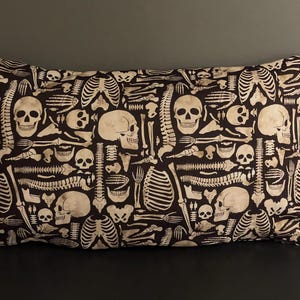 May include: A black pillow with a white skeleton pattern. The pattern includes skulls, bones, and ribs.