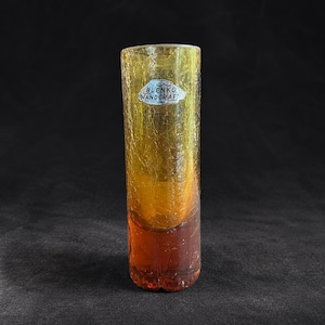 Pode incluir: Um vaso cilíndrico de vidro com textura craquelada, que transita de um amarelo âmbar claro no topo para um laranja profundo na base. Um autocolante prateado na parte superior do vidro apresenta a inscrição BLENKO HANDCRAFT.