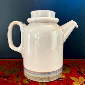May include: A white ceramic teapot with a brown and blue band around the bottom. The teapot has a lid and a handle.