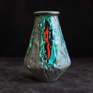 May include: A ceramic vase with a textured, matte grey exterior featuring a prominent vertical drip pattern. The glaze displays vibrant streaks of bright turquoise and bold red, accented by deep black patches that run down the centre of the body.