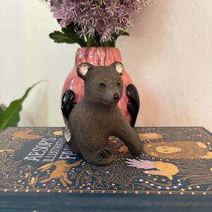May include: A small brown ceramic bear figurine with white accents sitting on a book titled "Aesop's Illustrated Fables".
