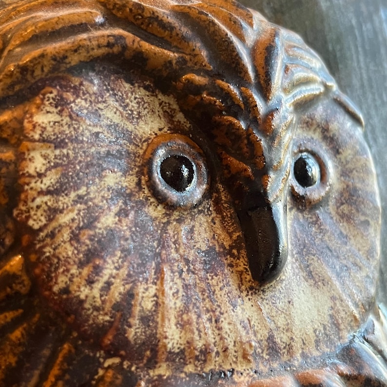 K&ouml;nnte beinhalten: Nahaufnahme einer Keramik-Eulen-Skulptur. Die Eule hat gro&szlig;e, dunkle Augen und eine detaillierte, strukturierte Oberfl&auml;che. Die Farbpalette umfasst Braunt&ouml;ne, Beige und Schwarz, was ein rustikales Aussehen erzeugt. Der Schnabel der Eule ist gl&auml;nzend schwarz.