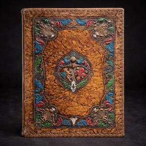 Könnte beinhalten: Ein braunes, ledergebundenes Notizbuch mit geprägten, farbenfrohen floralen und heraldischen Designs. Das Cover zeigt ein zentrales Emblem und einen dekorativen Rand mit roten, blauen, grünen und weißen Akzenten. Die Kanten sind genäht.