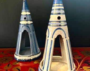 Könnte beinhalten: Zwei kerzenförmige Kerzenhalter aus Keramik mit blauen und goldenen Akzenten. Die Halter haben ein Ausschnittdesign und stehen auf einer roten Oberfläche mit einem Blumenmuster.