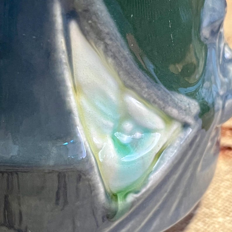 Pode incluir: Close-up de um objeto de cer&acirc;mica com acabamento brilhante. O objeto apresenta uma mistura de cores, incluindo tons de azul, verde e branco. O design tem uma apar&ecirc;ncia texturizada, com pinceladas vis&iacute;veis e sutis varia&ccedil;&otilde;es de cor. A est&eacute;tica geral &eacute; art&iacute;stica e artesanal.