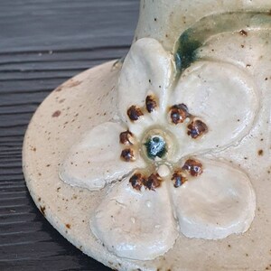 May include: A ceramic vase with a white glaze and a brown flower design. The flower has five petals and a brown center.