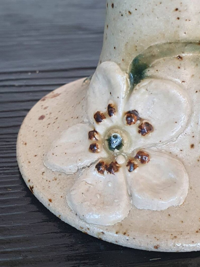 May include: A ceramic vase with a white glaze and a brown flower design. The flower has five petals and a brown center.