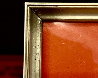 May include: Close-up of the top corner of a gold picture frame with a red background.