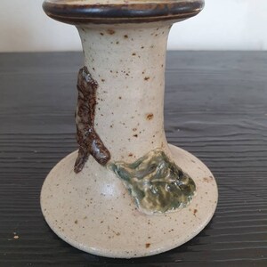 May include: A white ceramic candle holder with brown and green accents. The holder has a textured surface and a simple design.