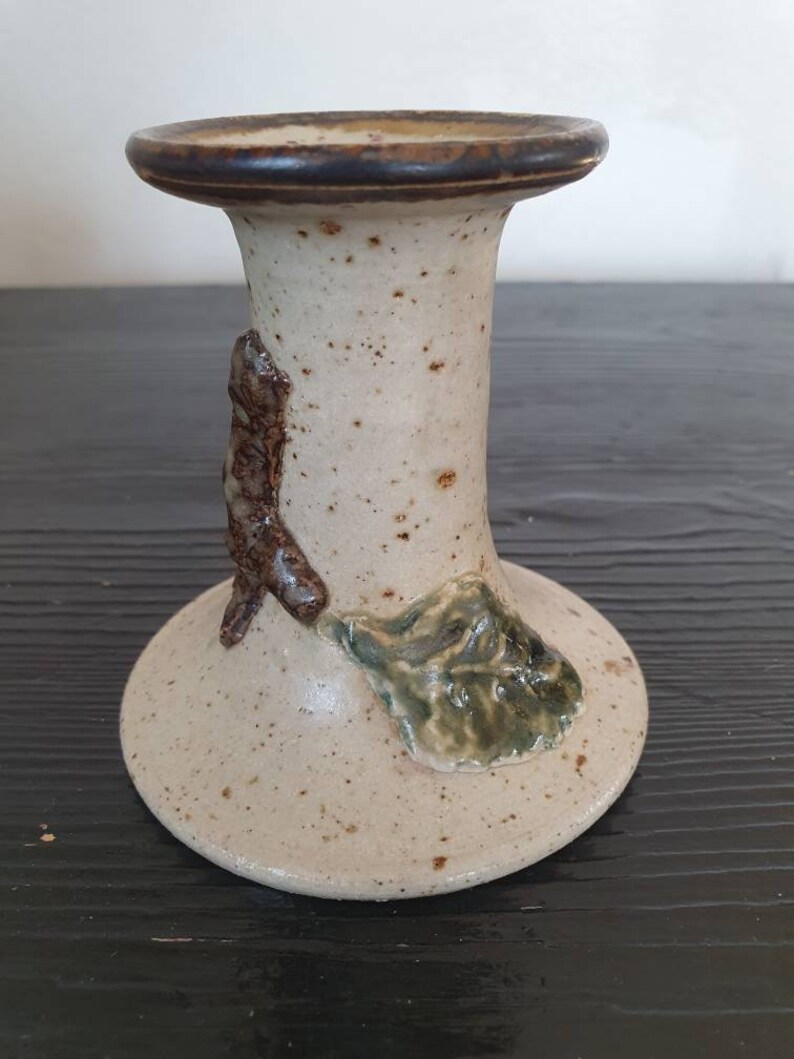 May include: A white ceramic candle holder with brown and green accents. The holder has a textured surface and a simple design.