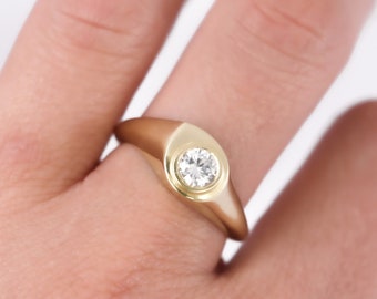 May include: A gold ring with a round, bezel-set diamond.