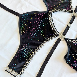 K&ouml;nnte beinhalten: Schwarzes Samt-Halter-Top mit Regenbogen-Stra&szlig;steinen und silbernen &Ouml;sen. Das Oberteil hat ein Kreuzband-Design und einen Blumenakzent.