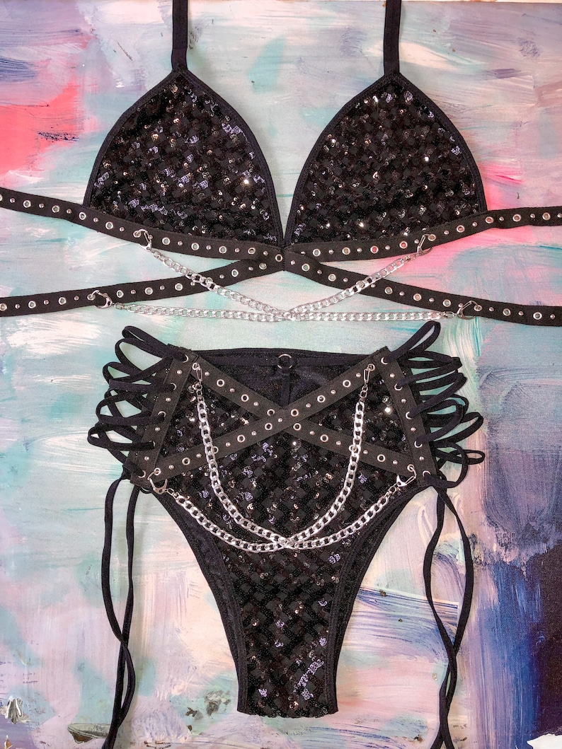 May include: Black sequined lingerie set with a triangle bra and high-waisted bottoms. The set features multiple straps and chains.