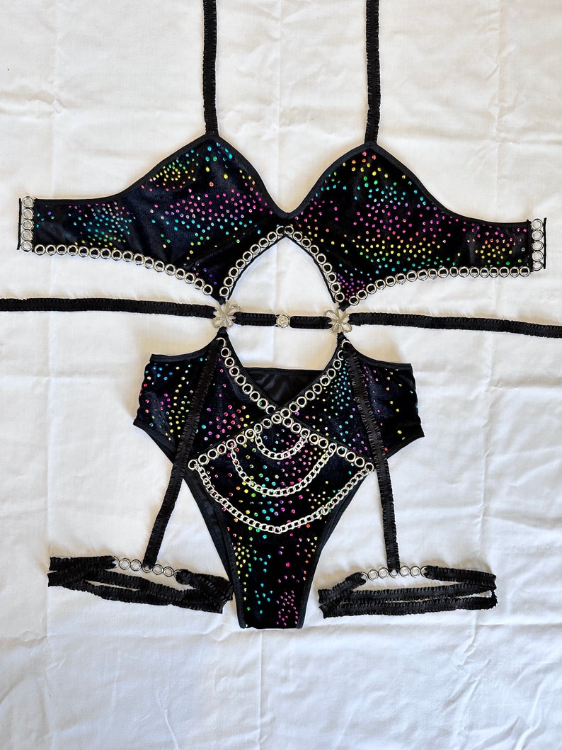 K&ouml;nnte beinhalten: Schwarzes Samt-Dessous-Set mit silbernen Ketten und bunten Strasssteinen. Das Set beinhaltet einen BH, einen Body und Str&uuml;mpfe.