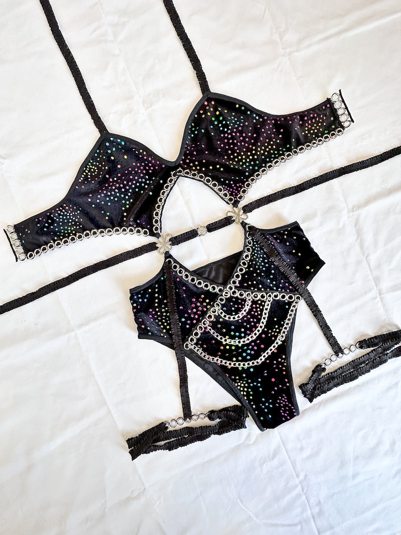 K&ouml;nnte beinhalten: Schwarzes Dessous-Set mit Regenbogen-Stra&szlig;steinen und silbernen Kettenakzenten. Das Set beinhaltet einen BH, einen Body und Str&uuml;mpfe.