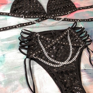 May include: Black sequined lingerie set with silver chains and grommets. The set includes a triangle bra and high-waisted bottoms with a criss-cross design.