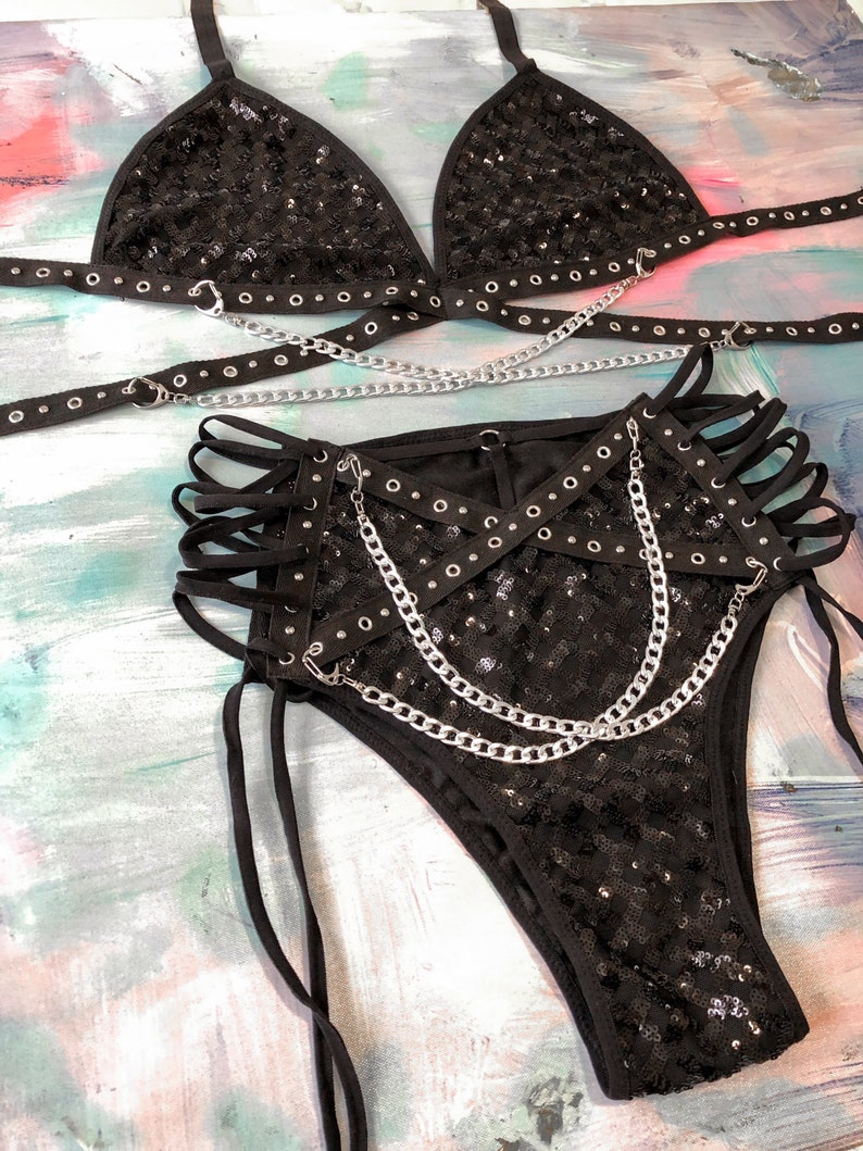 May include: Black sequined lingerie set with silver chains and grommets. The set includes a triangle bra and high-waisted bottoms with a criss-cross design.
