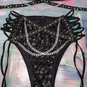 May include: Black sequined lingerie set with silver chains and black straps. The set includes a bra and a pair of bottoms with a high-cut leg.