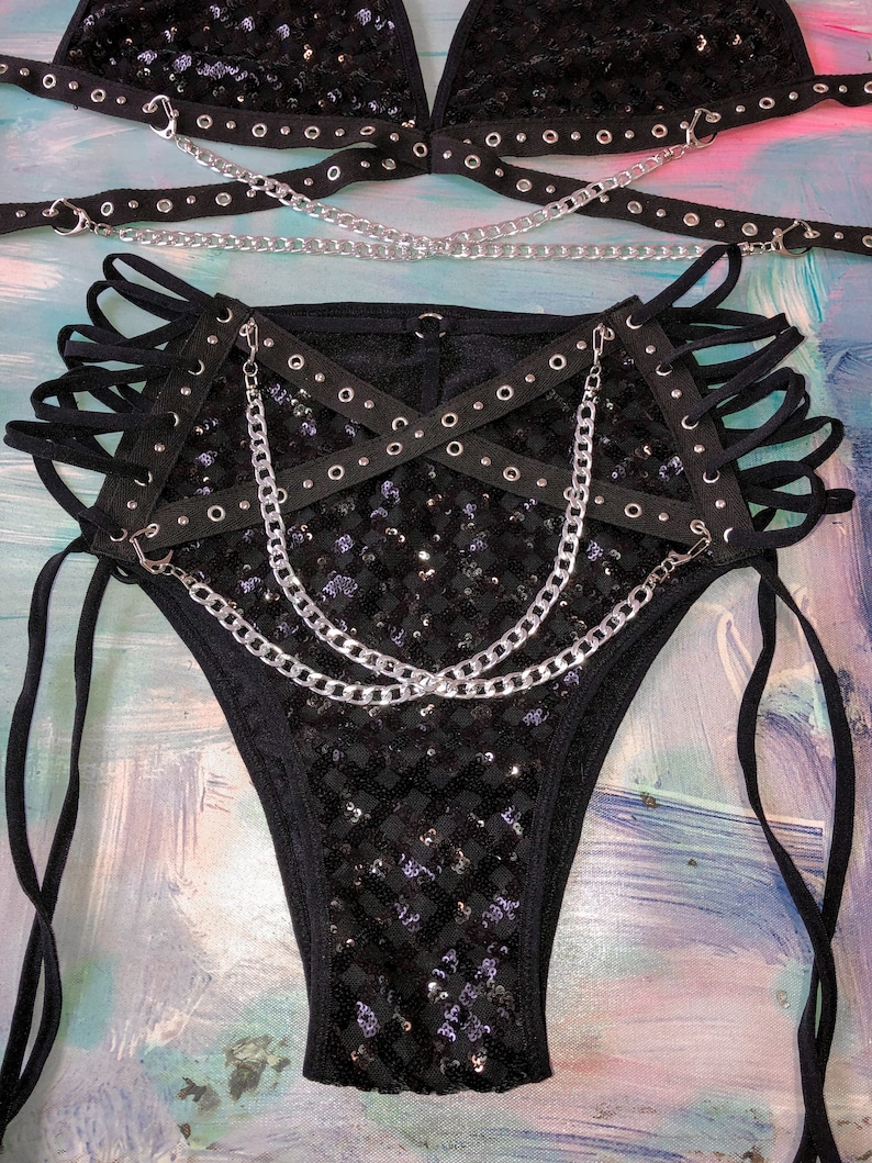 May include: Black sequined lingerie set with silver chains and black straps. The set includes a bra and a pair of bottoms with a high-cut leg.