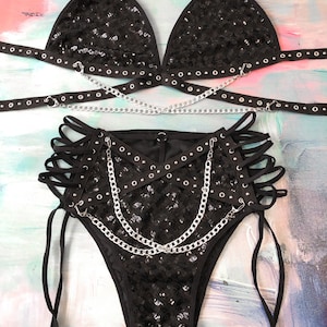 May include: Black sequined lingerie set with silver chains and grommets. The set includes a triangle bra and high-waisted bottoms with lace-up sides.