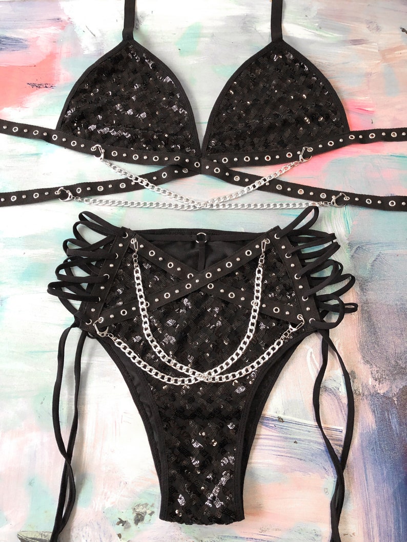 May include: Black sequined lingerie set with silver chains and grommets. The set includes a triangle bra and high-waisted bottoms with lace-up sides.