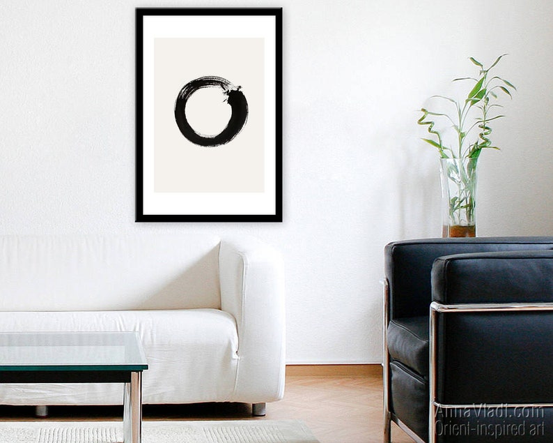 May include: A black and white minimalist art print featuring a single circle drawn in a brushstroke style. The circle is incomplete, creating a sense of movement and flow. The print is framed in a black frame and hangs on a white wall.