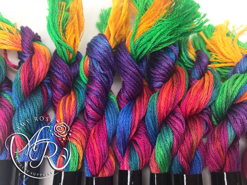 May include: A close-up of a collection of colorful embroidery floss spools. The floss is a mix of green, purple, orange, red, and blue. The spools are arranged in a row and are ready to be used for crafting projects.
