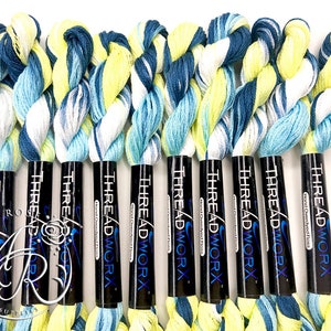 K&ouml;nnte beinhalten: Zehn Spulen handgef&auml;rbter Stickgarn in Blaut&ouml;nen, Wei&szlig; und Gelb. Jede Spule ist mit "THREADWORX Hand Dyed Floss" beschriftet.