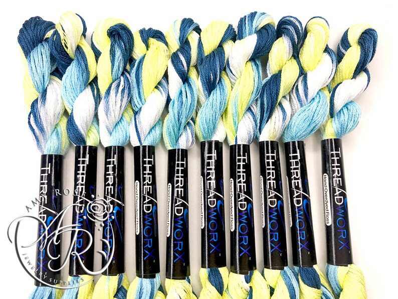 K&ouml;nnte beinhalten: Zehn Spulen handgef&auml;rbter Stickgarn in Blaut&ouml;nen, Wei&szlig; und Gelb. Jede Spule ist mit "THREADWORX Hand Dyed Floss" beschriftet.