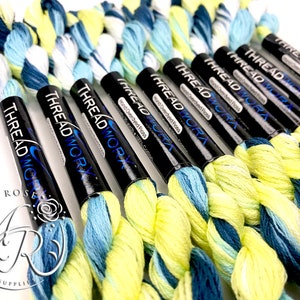 K&ouml;nnte beinhalten: Nahaufnahme von acht Spulen handgef&auml;rbter Stickgarn in Blaut&ouml;nen, Gr&uuml;n- und Gelbt&ouml;nen. Die Spulen sind mit "THREAD WORK" und "Hand Overdyed Floss" beschriftet.