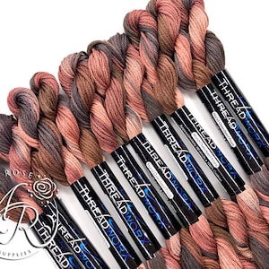 May include: A close-up of eight spools of embroidery floss in a gradient of brown, pink, and gray. The spools are labeled "THREADWORX" and "Hand Overdyed Floss".