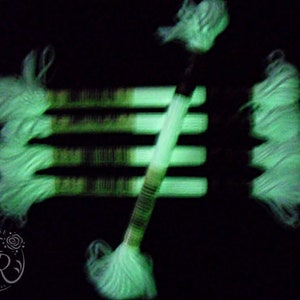 May include: Five spools of glow-in-the-dark embroidery floss in a light green color. The floss is arranged in a fan shape, with the ends of the spools facing the viewer.