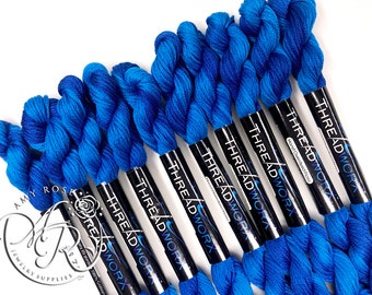 May include: A close-up of six spools of blue and dark blue hand-dyed embroidery floss. The spools are labelled "THREADWORX Hand-Overdyed Floss 20 yard 100% Cotton".
