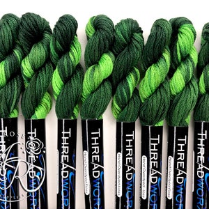 Op de afbeelding: Tien spoelen handgeverfde floss in groen en limoengroen, elk met het label "THREADWOR Hand Overdyed Floss".