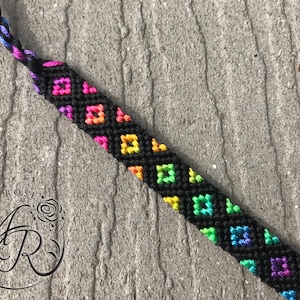 May include: A black friendship bracelet with a rainbow diamond pattern.