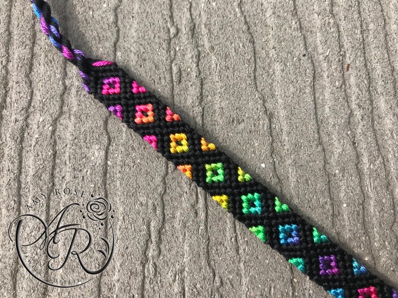May include: A black friendship bracelet with a rainbow diamond pattern.