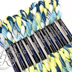 K&ouml;nnte beinhalten: Ein Set mit zehn Kn&auml;uel Stickgarn in einem Farbverlauf von Blau, Wei&szlig; und Gelb. Das Garn ist auf schwarzen Spulen aufgewickelt, auf denen der Text "THREAD WORX" gedruckt ist.