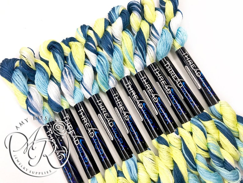 K&ouml;nnte beinhalten: Ein Set mit zehn Kn&auml;uel Stickgarn in einem Farbverlauf von Blau, Wei&szlig; und Gelb. Das Garn ist auf schwarzen Spulen aufgewickelt, auf denen der Text "THREAD WORX" gedruckt ist.