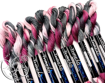 Può includere: Primo piano di otto rocchetti di filo da ricamo tinto a mano. Il filo è un mix di rosa, grigio e bordeaux. I rocchetti sono etichettati con "THREADWORX" e "Filo tinto a mano".