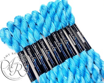 May include: A close-up of six spools of light blue hand-overdyed floss, each spool is labelled "THREADWORX" and "Approximately 20 yards - 100% Cotton".