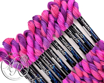 Può includere: Una collezione di rocchetti di filo da ricamo rosa e viola con il nome del marchio "THREADWORX" stampato sulle etichette nere.